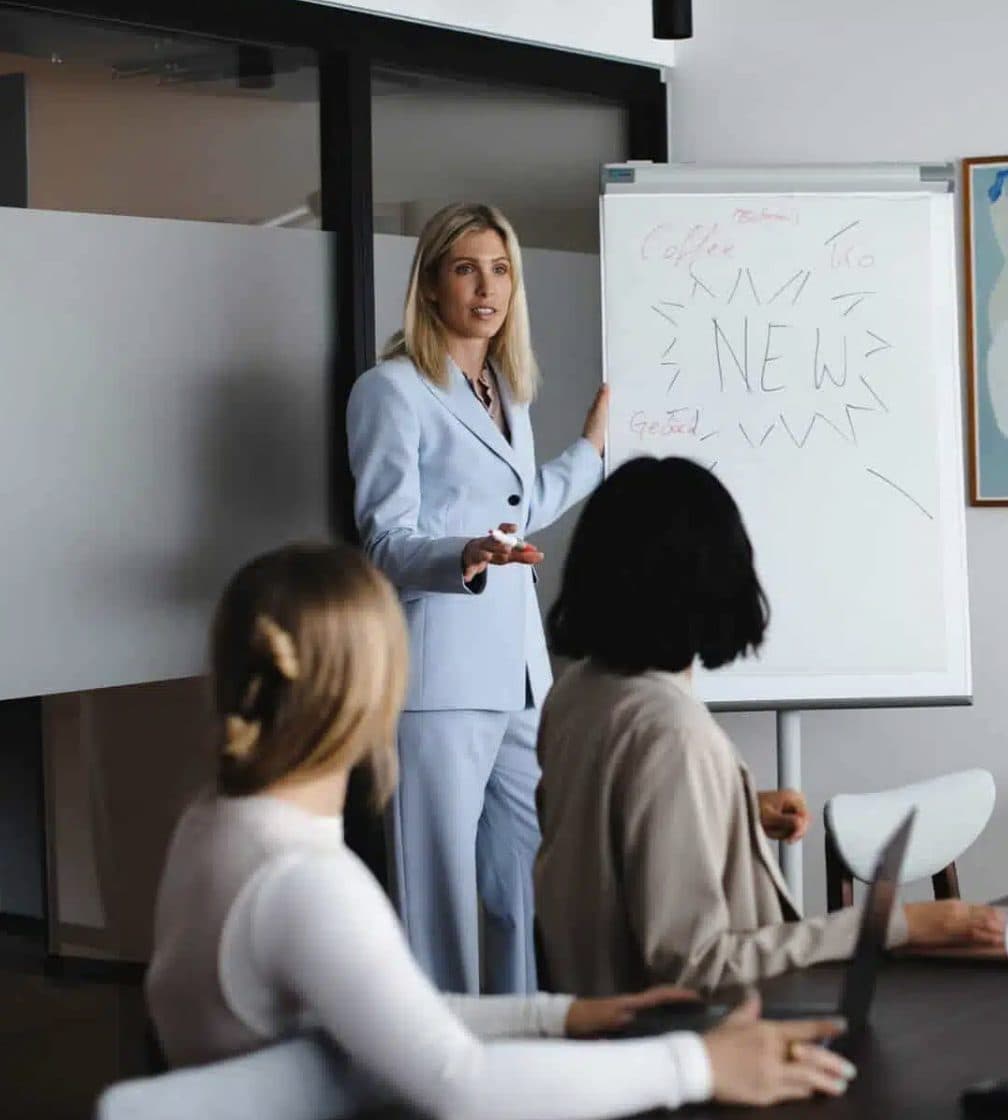 Eine Frau stellt zwei Kolleginnen in einem Besprechungsraum Ideen am Flipchart vor.